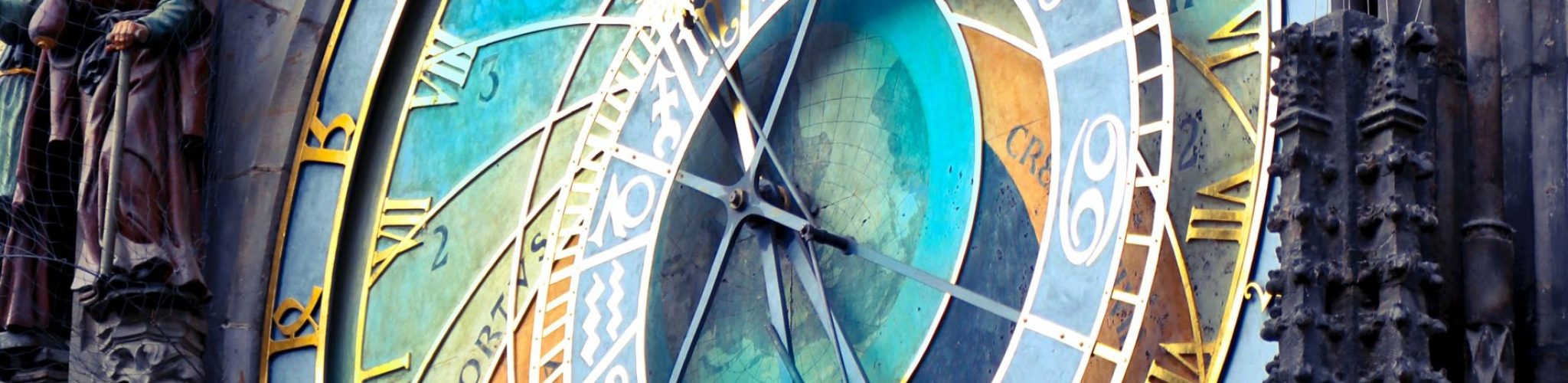 Detalle del Reloj Astronómico de Praga con sus complejos diales, agujas doradas, figuras animadas de la Muerte y otros personajes, incrustado en una estructura gótica.